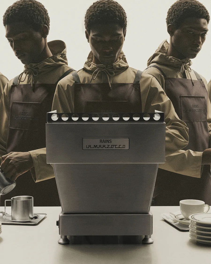 Baristas in der Schürze von Rains und La Marzocco an einer Linea Mini mit Rains-Schild