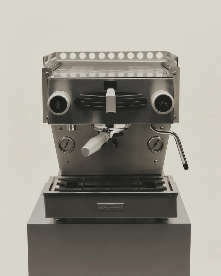 Linea Mini von Officine Fratelli Bambi aus der Zusammenarbeit von La Marzocco und Rains, mit Rains-Schild auf einem Sockel