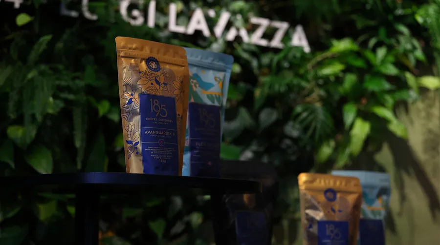 Kaffeepackungen von 1895 Coffee Designers by Lavazza vor einer begrünten Wand mit dem Lavazza-Schriftzug